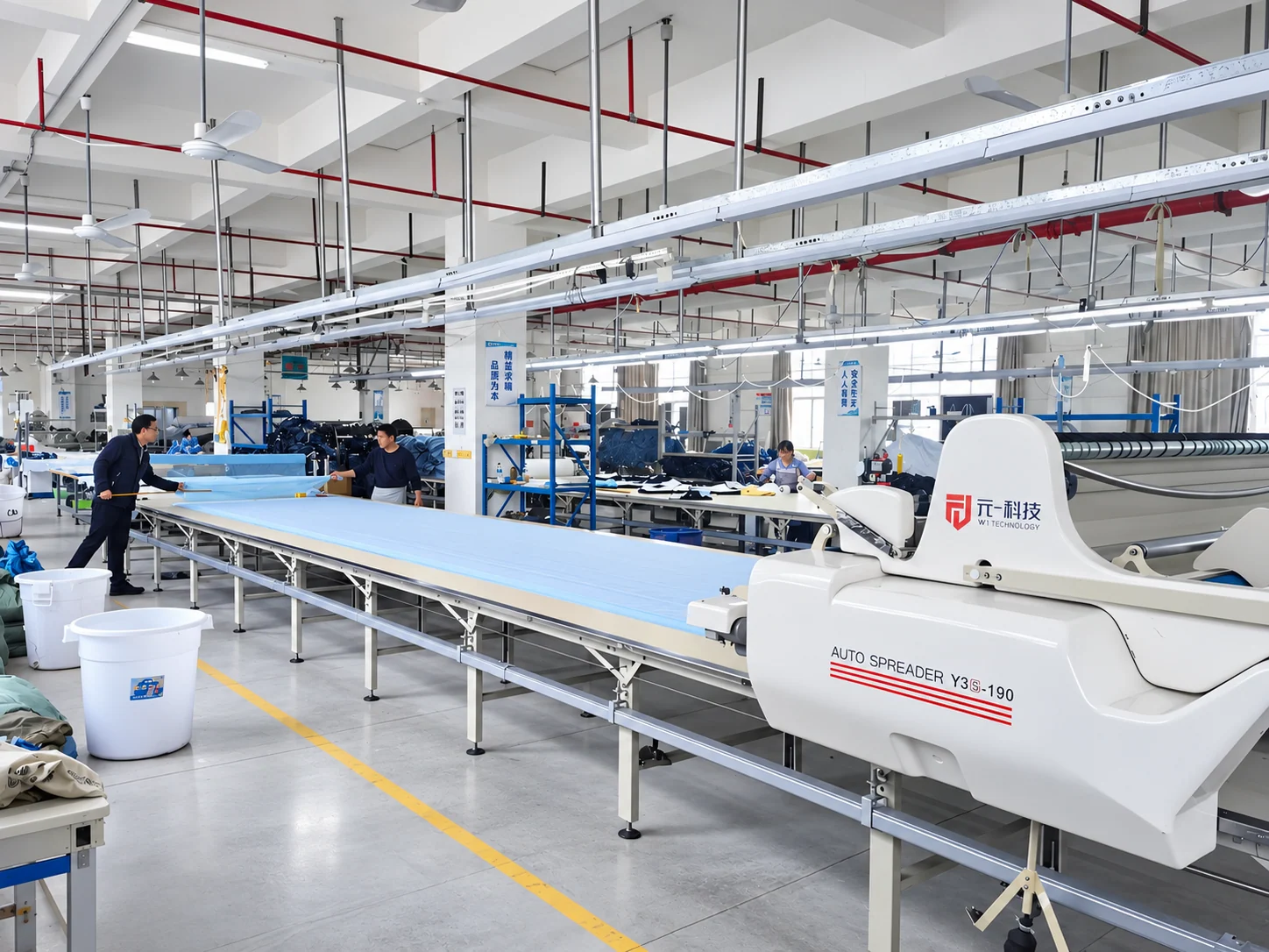 Fabric being laid out on a long table with an automatic spreading machine.