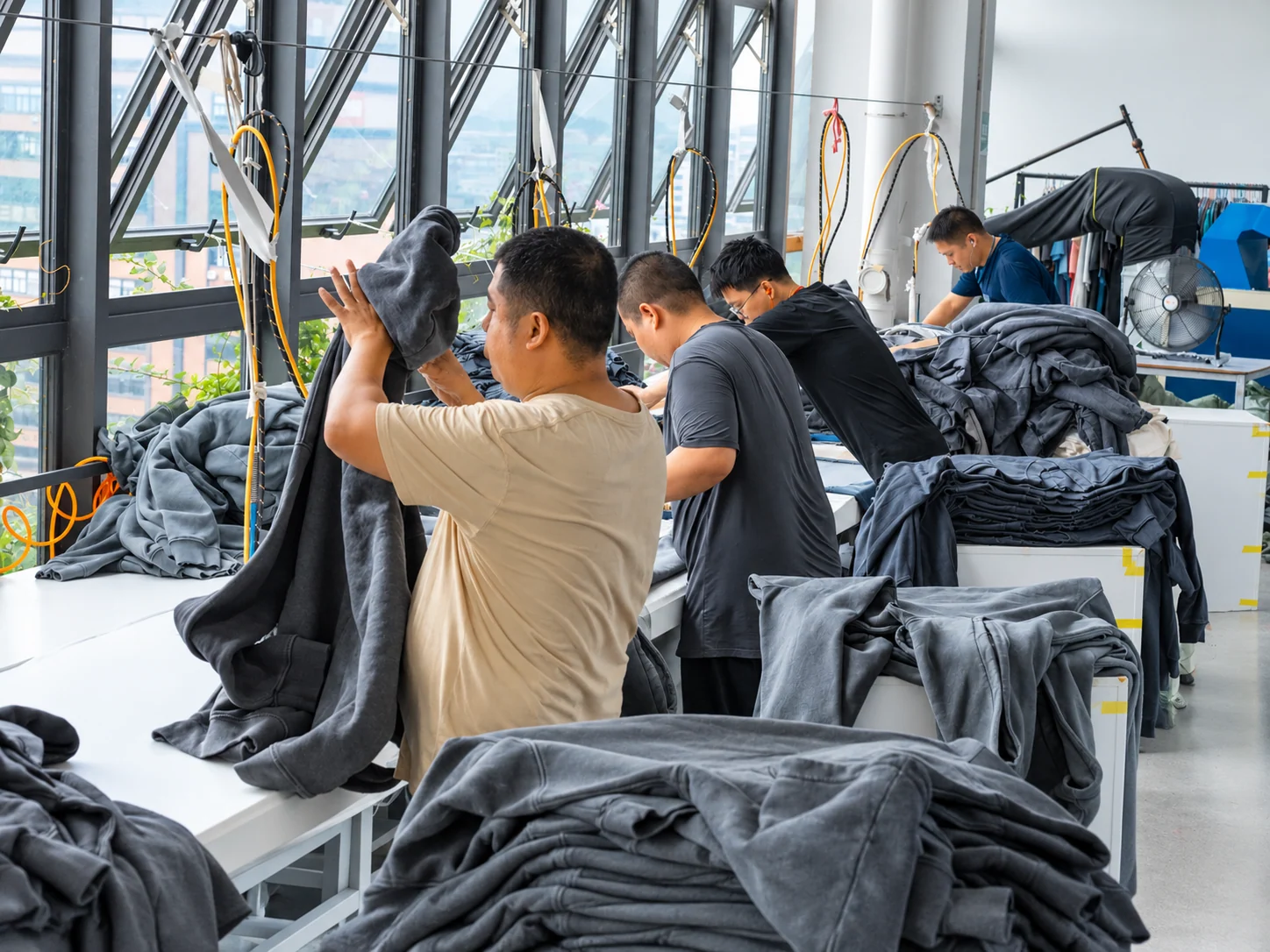 Team members inspecting and finishing grey garments at worktables.