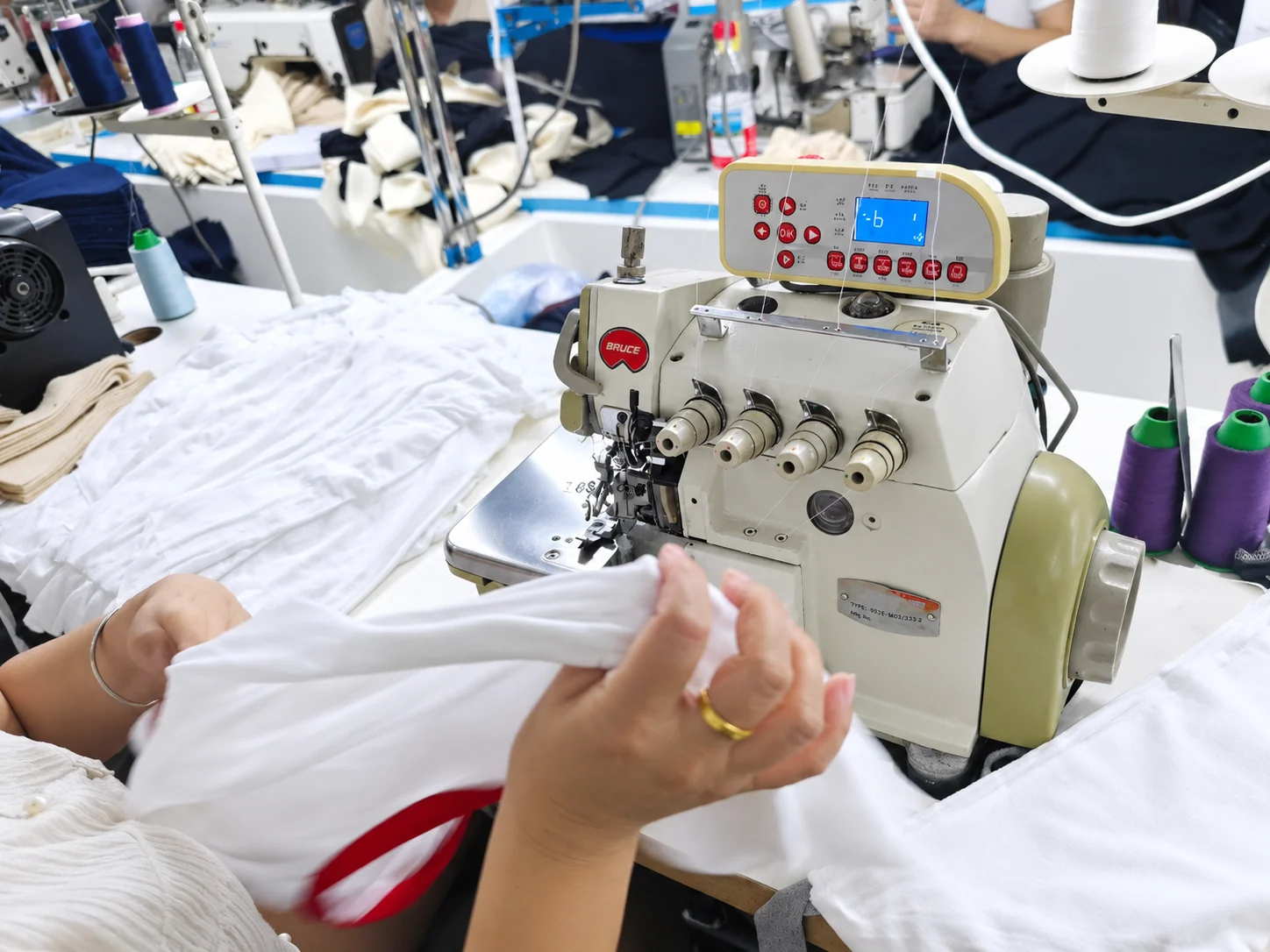 Close-up of an operator finishing a white garment at an overlock machine.